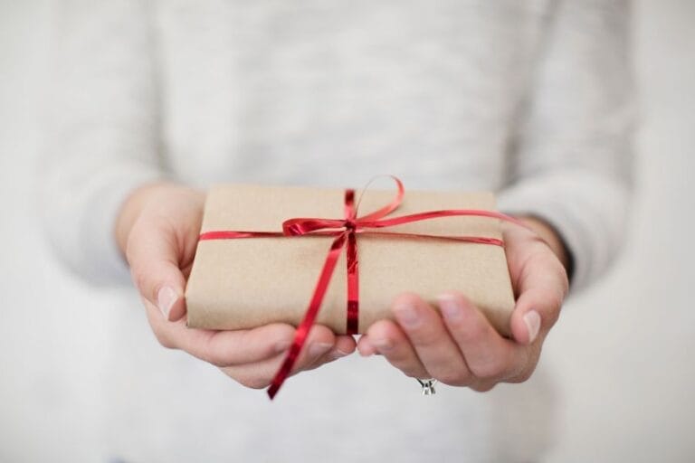 Hands holding a small gift wrapped in brown paper with a red ribbon, symbolizing the simple joy of Christ centered Christmas giving.