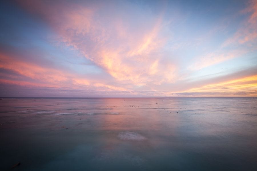 Peaceful sunrise over a calm ocean, with soft pink and blue clouds reflecting God's beauty and reminding us of His faithful care in Matthew 6:25–34.