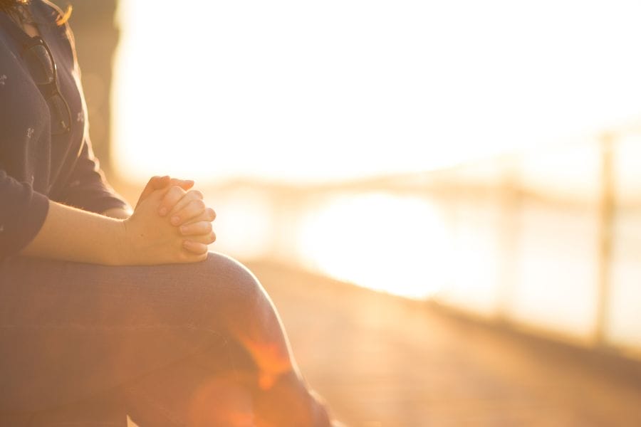Woman sitting quietly by the water at sunset, reflecting on slowing down and reclaiming ordinary life.