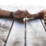 Husband and wife holding hands across a rustic wooden table, each with a coffee mug, symbolizing love, connection, and quiet encouragement in marriage.