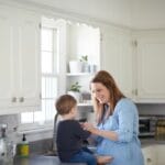 Mother smiling and spending time with her young child in a bright, cozy kitchen, reflecting warmth, love, and the joy of homemaking.