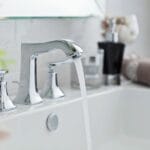 Clean white bathroom sink with running water, chrome faucet, and neatly folded towels—fresh and simple space ready after a deep clean