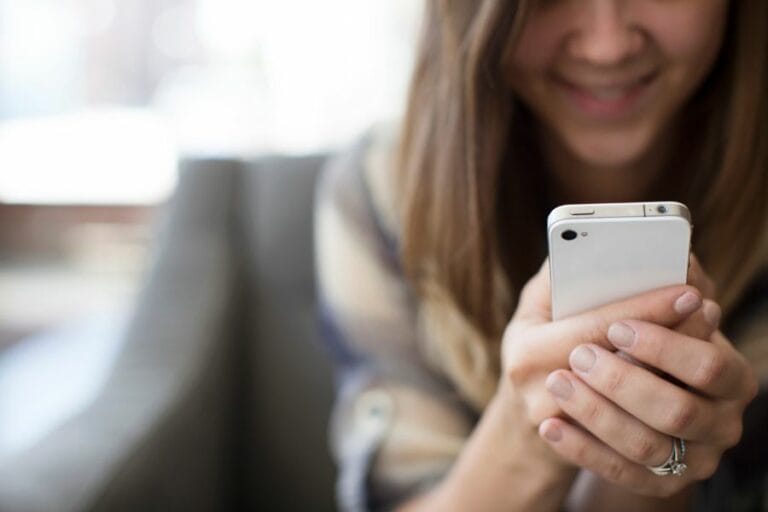 Smiling woman holding a smartphone, representing common distractions in daily homemaking tasks.
