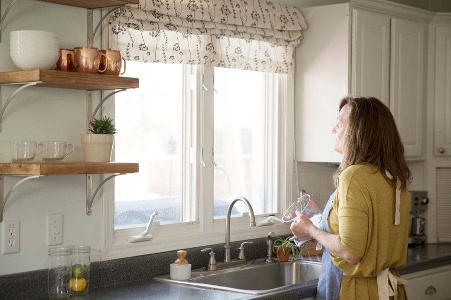 A woman washing dishes at her kitchen sink and looking out the window, reflecting the quiet, everyday ministry that happens in the home.
