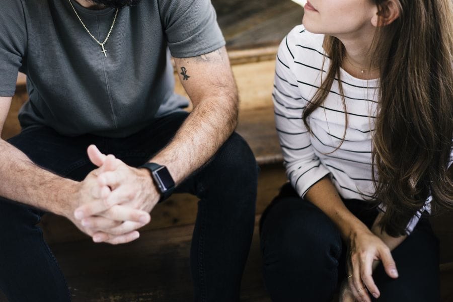 A Christian husband and wife sitting on wooden steps in serious conversation, reflecting on grace and biblical responses to sin in marriage.